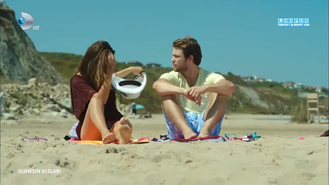 Hande Erçel sitting barefoot beside a man on a beach in a scene.