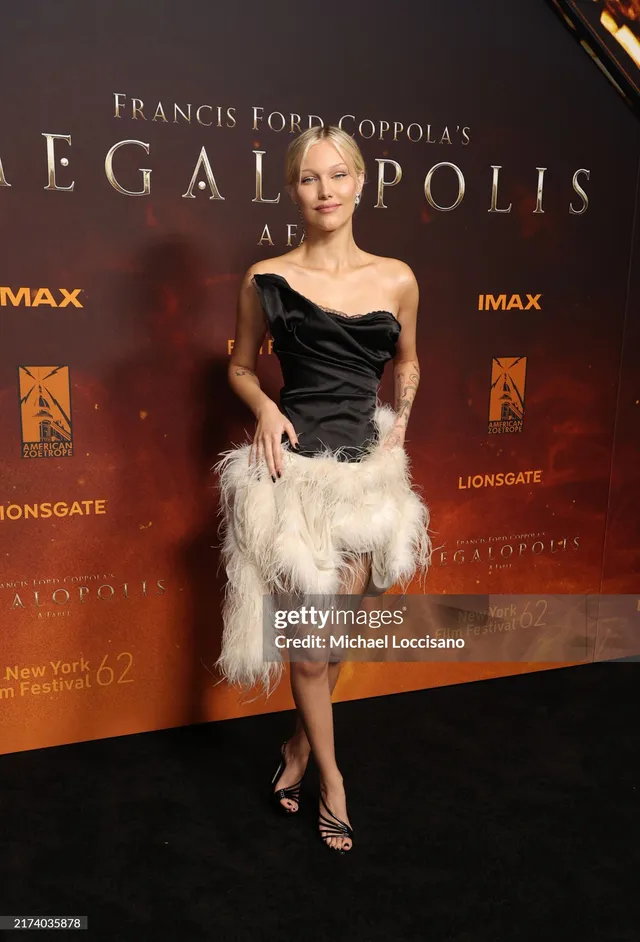 Grace VanderWaal posing in a feathered dress and heeled sandals at a premiere.