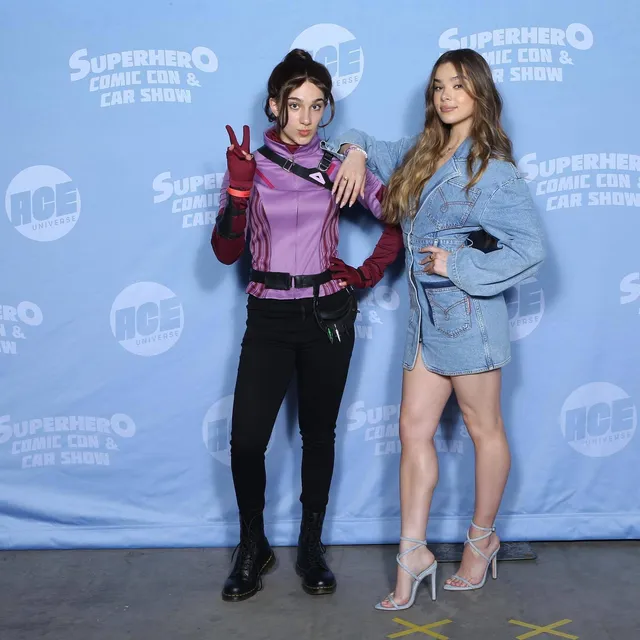 Hailee Steinfeld posing beside another performer in a denim outfit and clear heels.