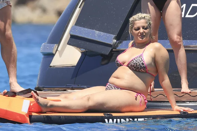 Bebe Rexha sitting barefoot on a paddleboard beside a boat.