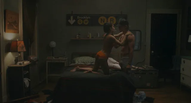 Zoë Kravitz sitting in a dimly lit bedroom scene.