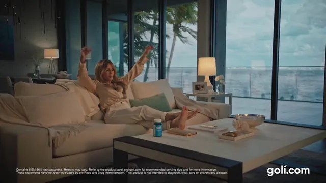 Jennifer Lopez relaxing barefoot on a sofa in a bright living room.