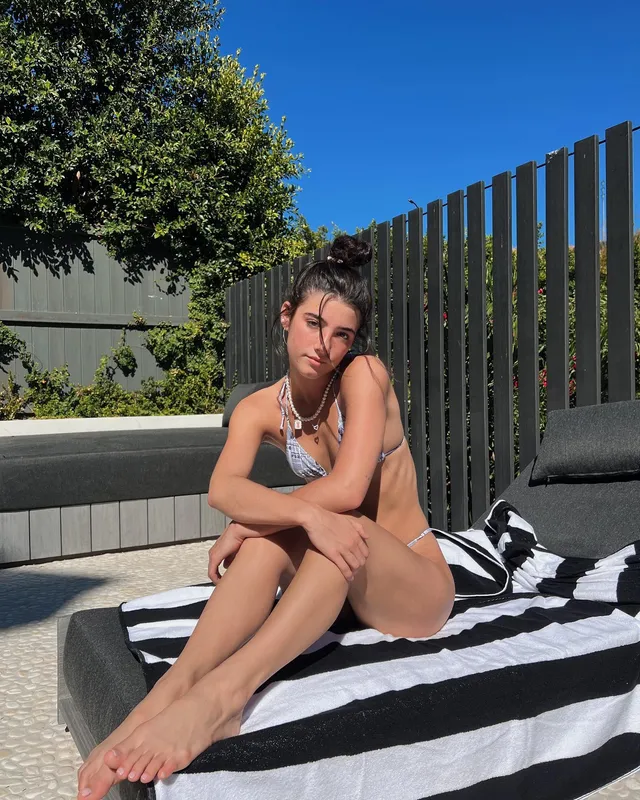 Charli D’Amelio sitting barefoot on a poolside lounger.