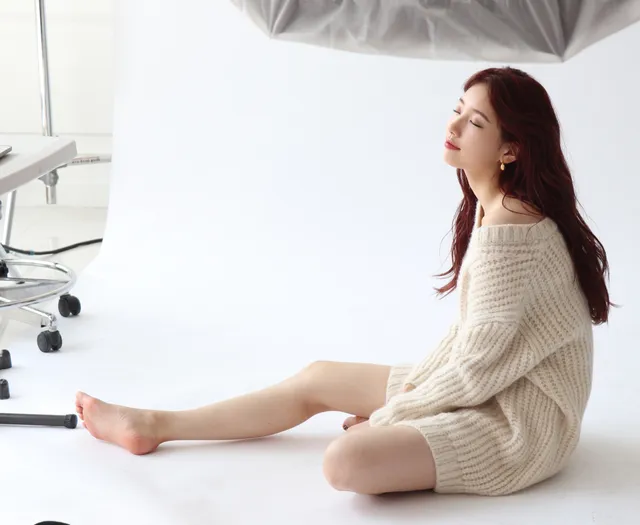 Bae Suzy sitting barefoot in a cream knit outfit.