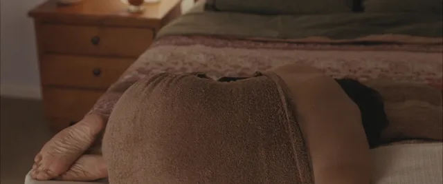 Elizabeth Olsen resting on a bed beneath a brown blanket.
