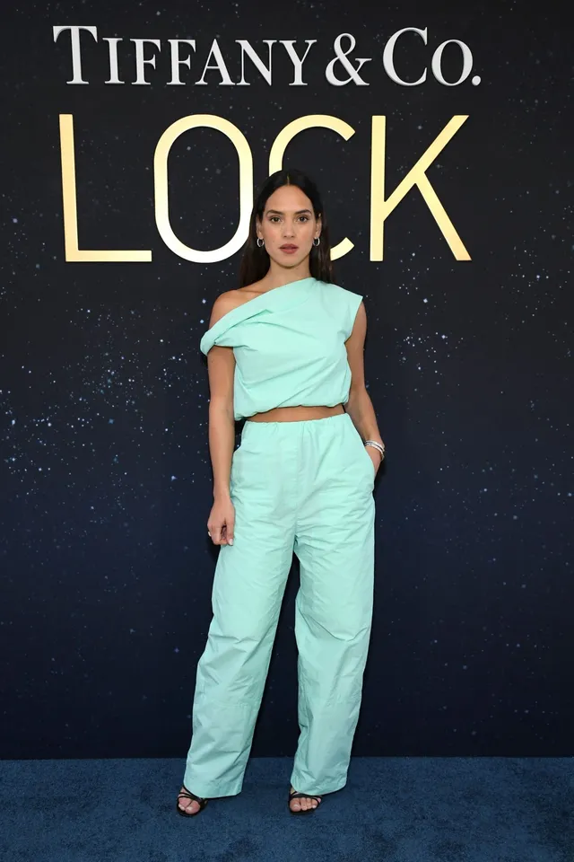 Adria Arjona posing in a mint outfit and dark heels at an event.