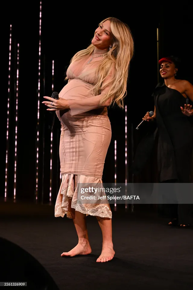 Ellie Goulding standing barefoot on stage in a pale dress.