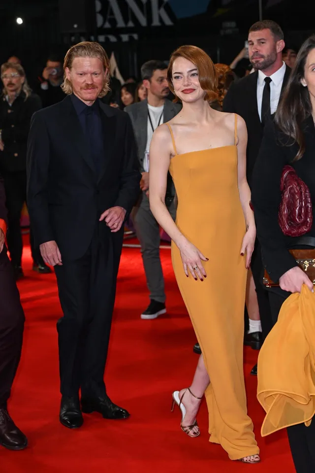 Emma Stone standing on a red carpet in a yellow gown and pale heels.