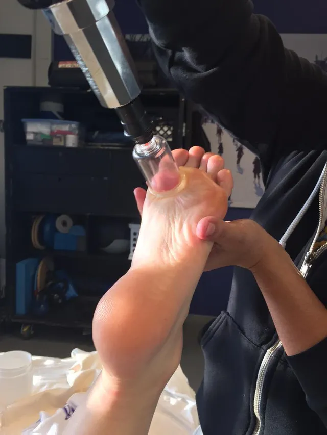 Katy Perry raising a bare sole while seated in a makeup chair.