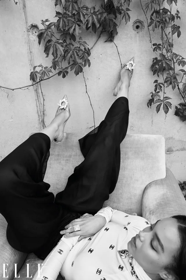 Whitney Peak reclining on a sofa in black trousers and metallic heels for a monochrome portrait.