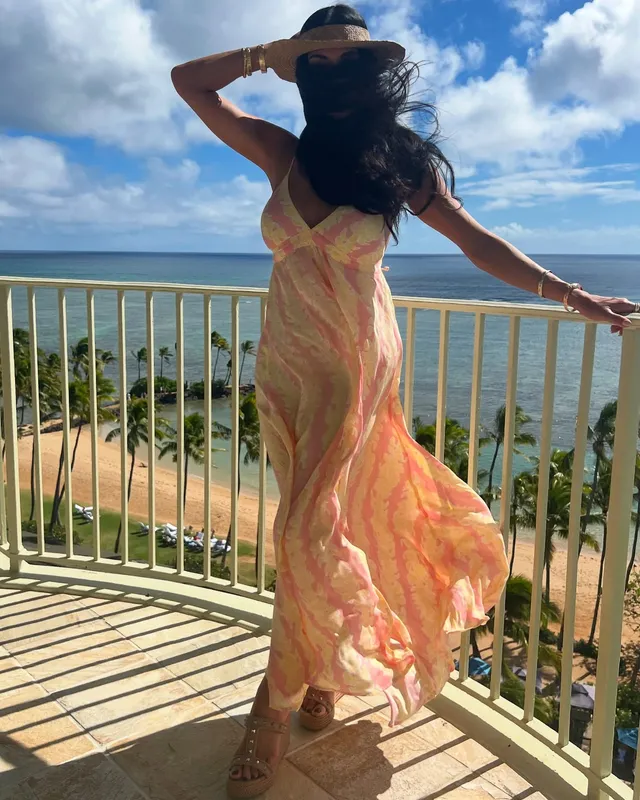 Nicole Scherzinger standing on a balcony in a flowing floral dress and platform heels.