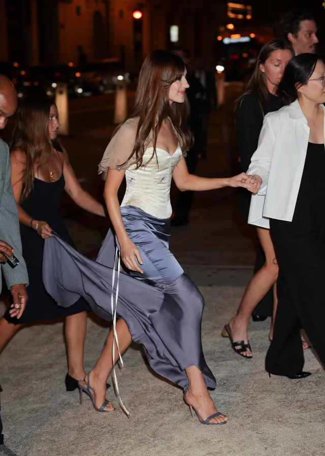 Daisy Edgar-Jones walking outdoors in a purple skirt and heels.