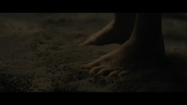 Daisy Ridley standing on sand in a screen scene.