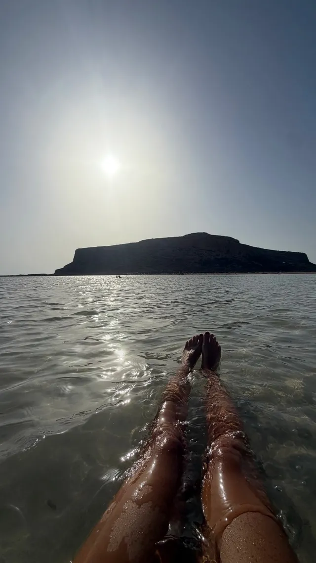 Emily Ratajkowski extending bare feet over sunlit seawater.