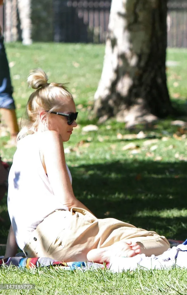 Gwen Stefani sitting barefoot on grass in a park.