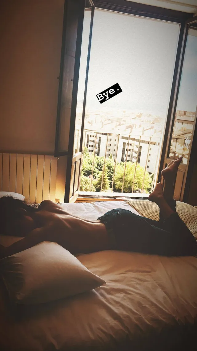 María Pedraza reclining barefoot on a bed beside an open doorway.