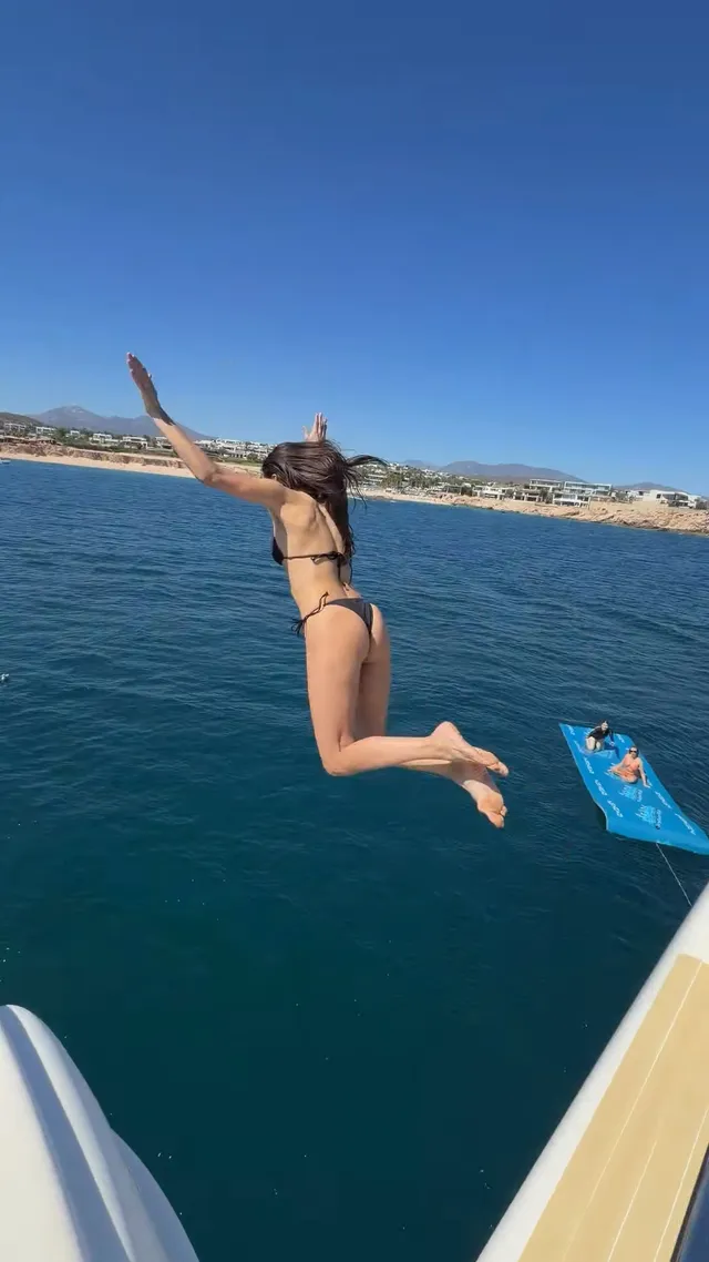 Nina Dobrev jumping barefoot from a boat toward blue water.