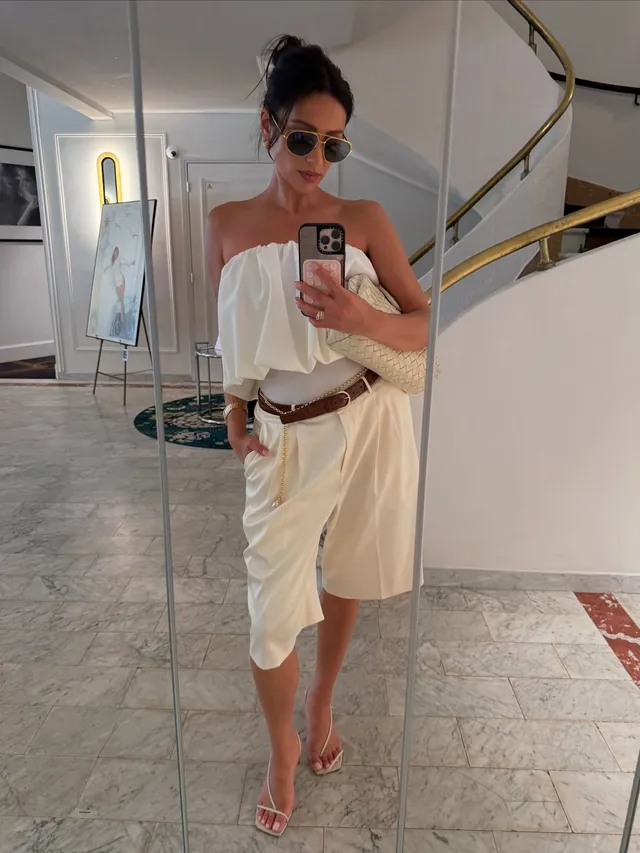 Shay Mitchell taking a mirror portrait in a cream outfit and sandals.