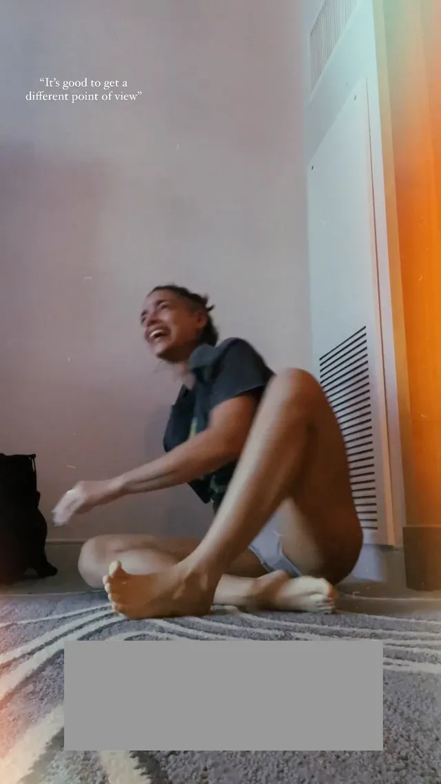 María Gabriela de Faría sitting barefoot and smiling on a mat.