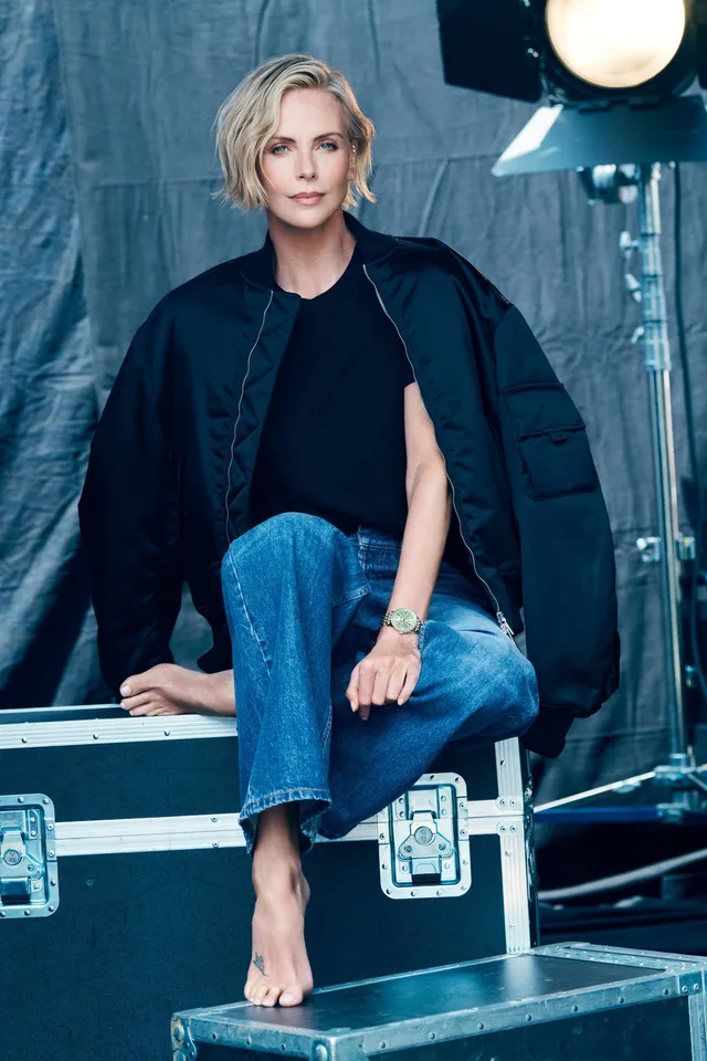 Charlize Theron seated on a backstage equipment case in jeans.