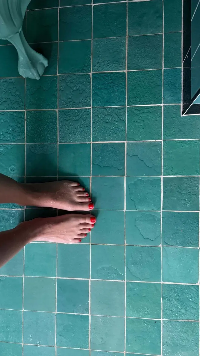 Emily Ratajkowski showing bare feet against green bathroom tiles.