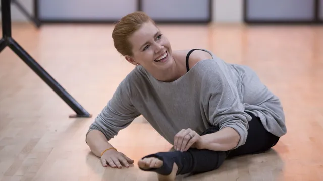 Amy Adams sitting on a studio floor in a casual outfit.
