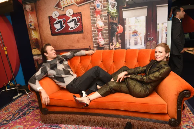 Willa Fitzgerald sitting barefoot on an orange sofa during an interview.