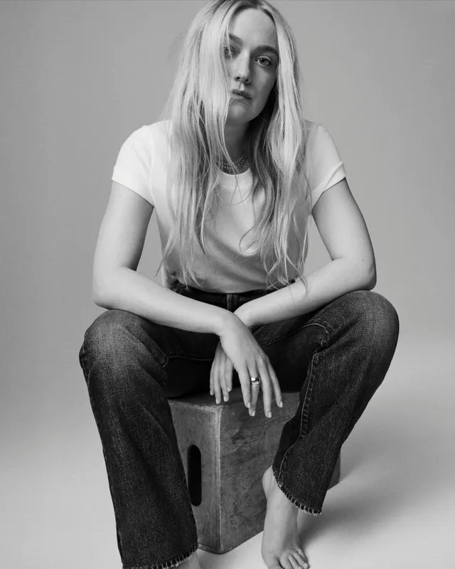 Dakota Fanning sitting barefoot for a black and white portrait in jeans and a white shirt.