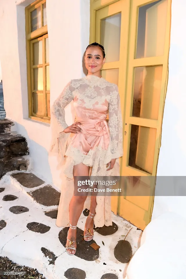 Nathalie Emmanuel posing by a yellow doorway in a pale pink dress.