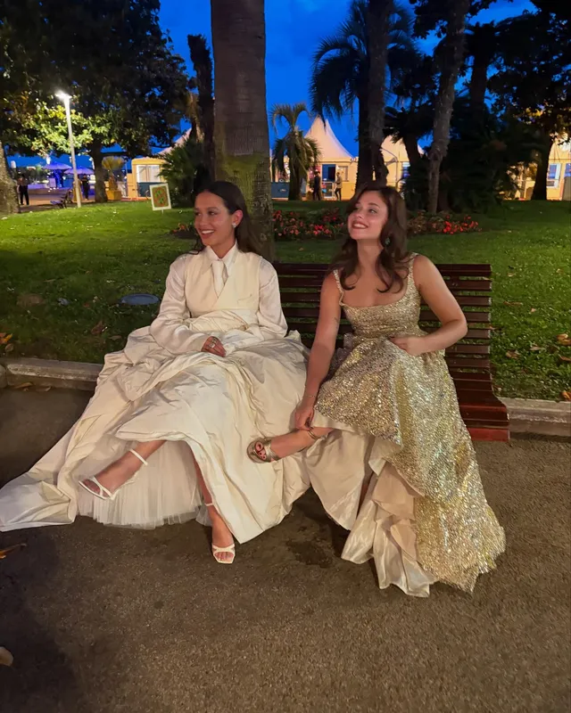 Nicole Wallace sitting beside a friend on a bench in a long pale gown and white heels.