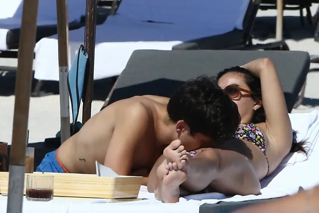 Camila Mendes relaxing beside a friend on a white lounger.