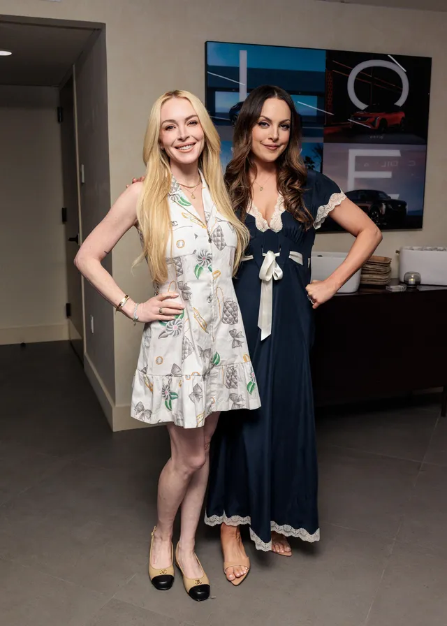 Elizabeth Gillies posing with a companion indoors in a navy dress.
