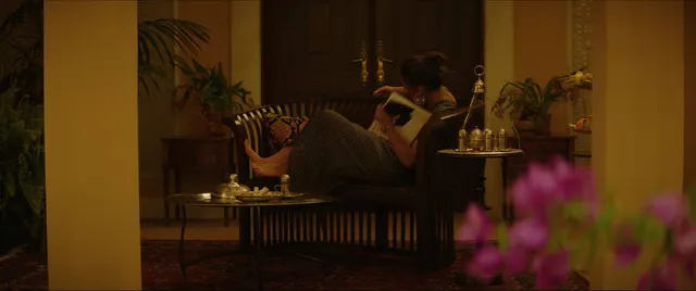 Naomi Scott sitting barefoot on a chair in a screen scene.