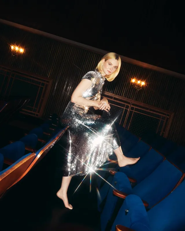Elle Fanning sitting barefoot in a theater wearing a silver dress.