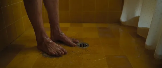 Melissa Barrera standing barefoot on a tiled bathroom floor.
