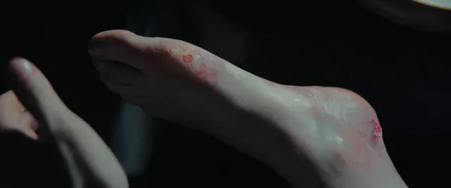 Daisy Ridley resting a bare foot in a dimly lit screen scene.