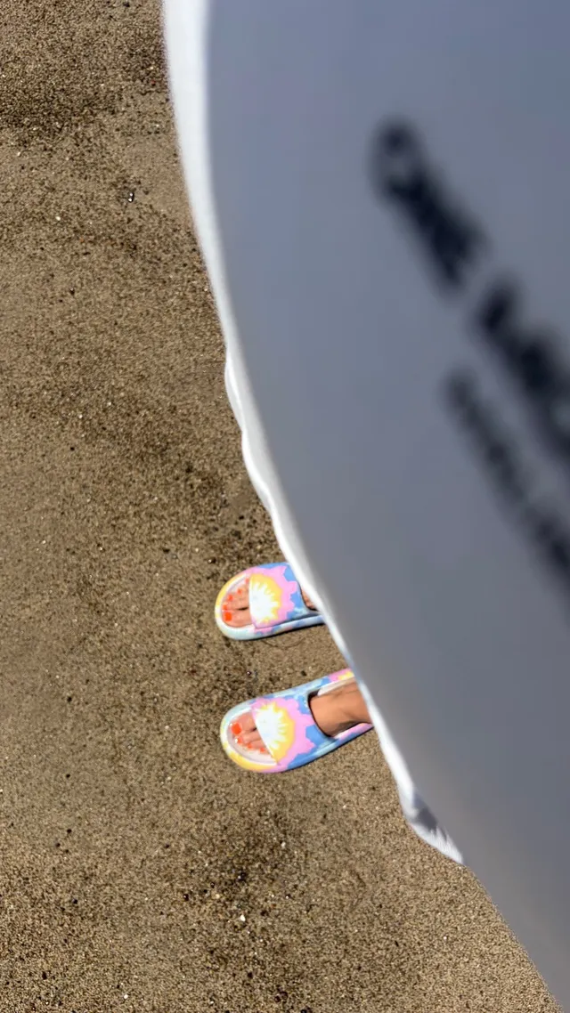 Alice Eve wearing colourful flat slides on sand.