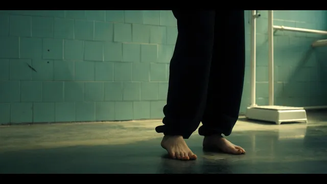Grace Van Patten walking barefoot across an indoor floor in a film scene.