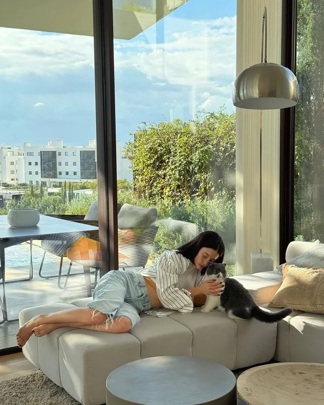 María Pedraza reclining barefoot on a sofa beside a cat.
