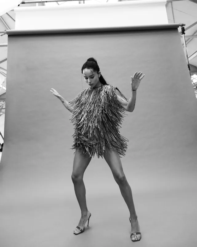 Zoë Kravitz posing in a fringed outfit in a monochrome studio photograph.