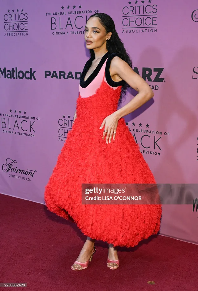 Tessa Thompson turning toward cameras in a red dress.