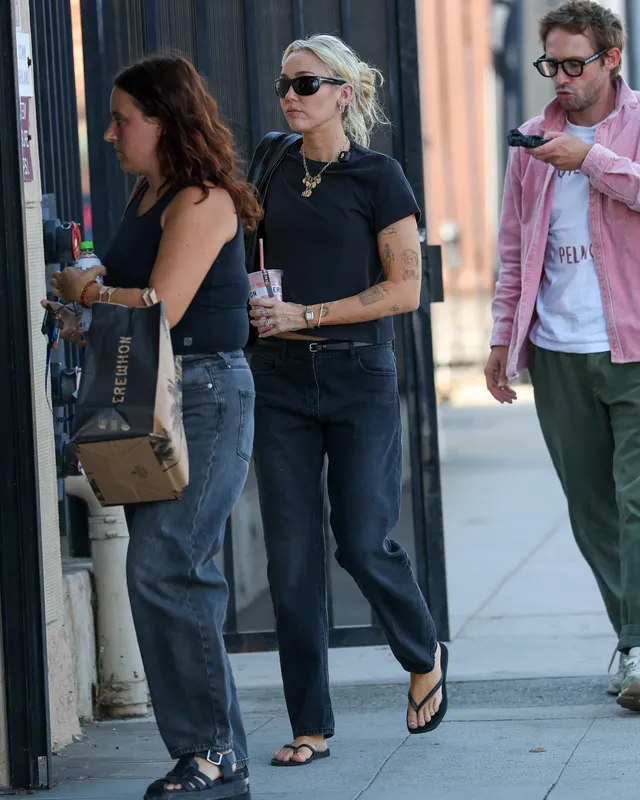 Miley Cyrus walking outside in jeans and flip-flops.