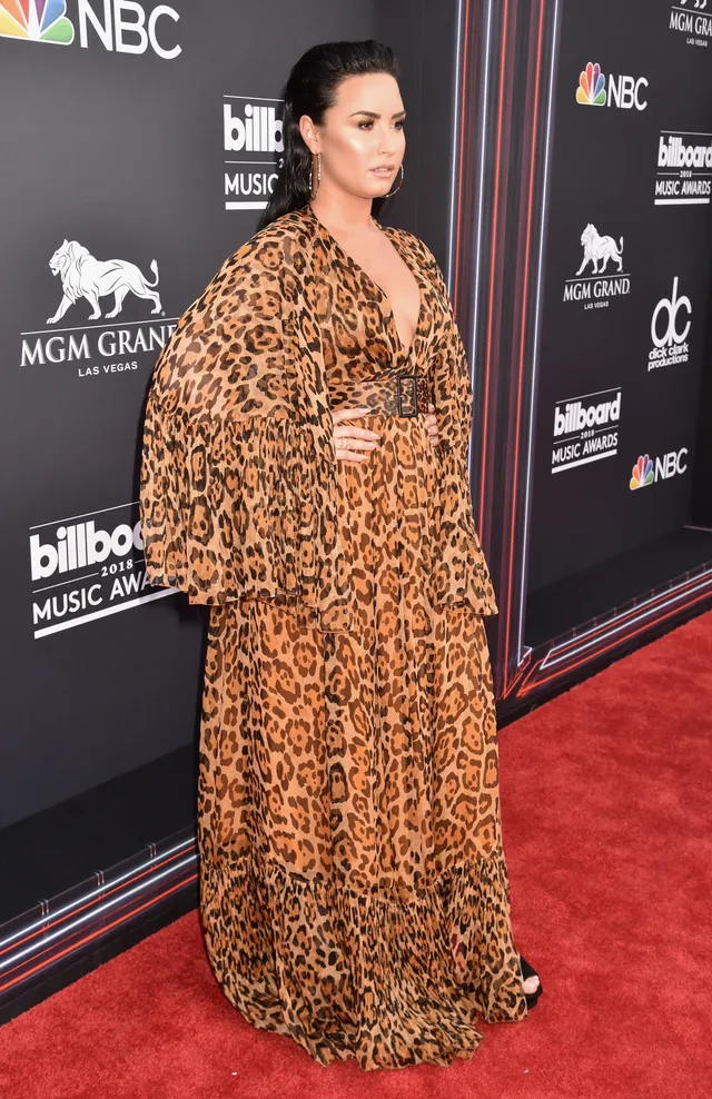 Demi Lovato posing at an event in a patterned gown and black heels.