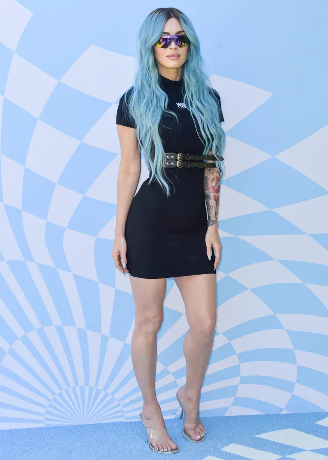 Megan Fox standing beside an event backdrop in a black outfit.
