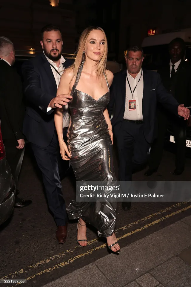 Jodie Comer walking among guests in a metallic gown.