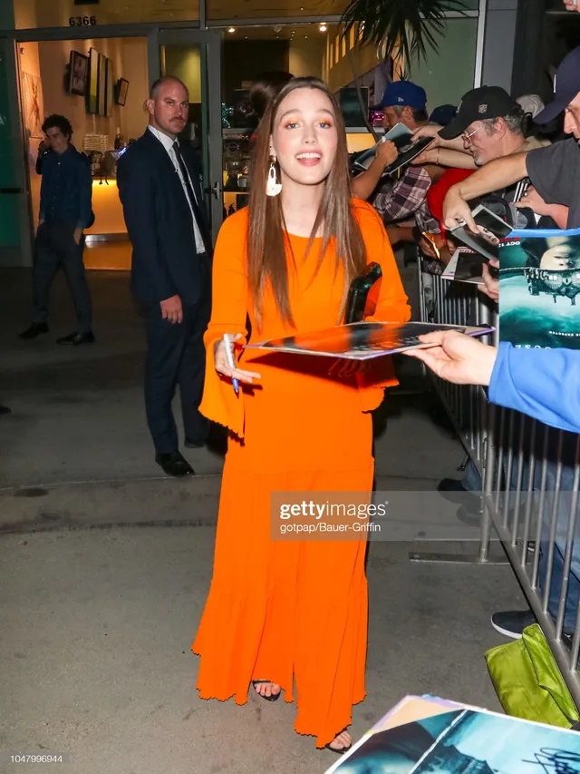 Victoria Pedretti greeting fans outside a premiere in an orange dress.
