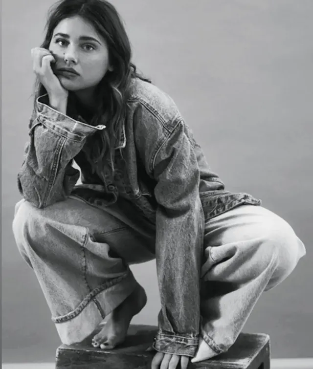 Nicole Wallace crouching barefoot in a denim outfit for a monochrome portrait.