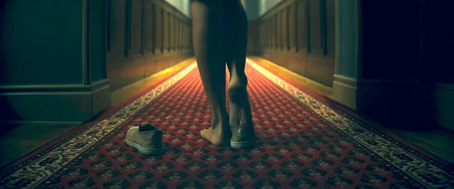 Ester Expósito showing her bare feet in a dimly lit hallway scene.
