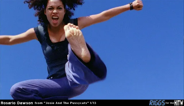 Rosario Dawson posing in a blue outfit with one foot raised.