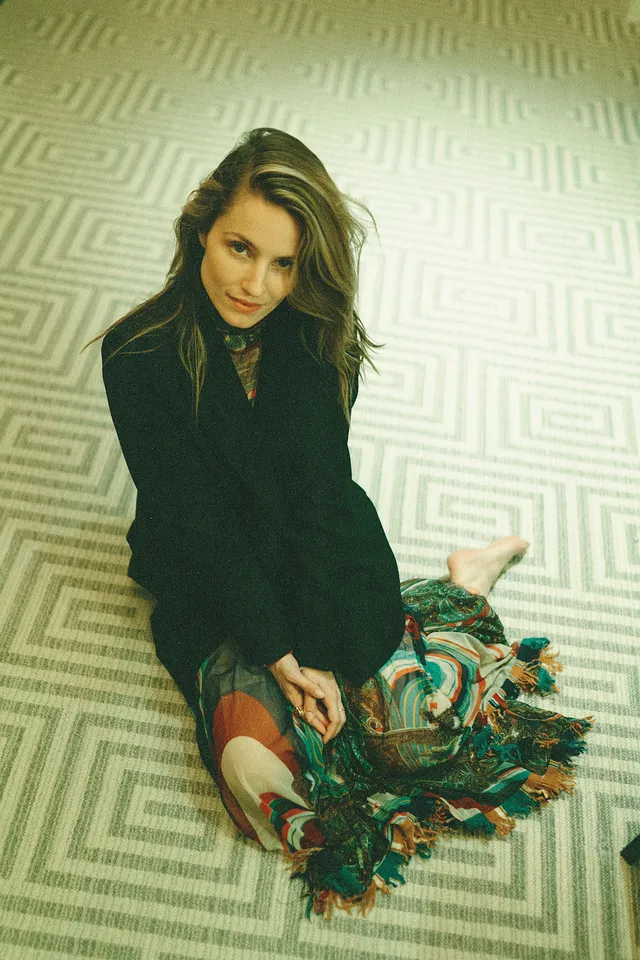 Dianna Agron sitting for a fashion portrait in a dark outfit.